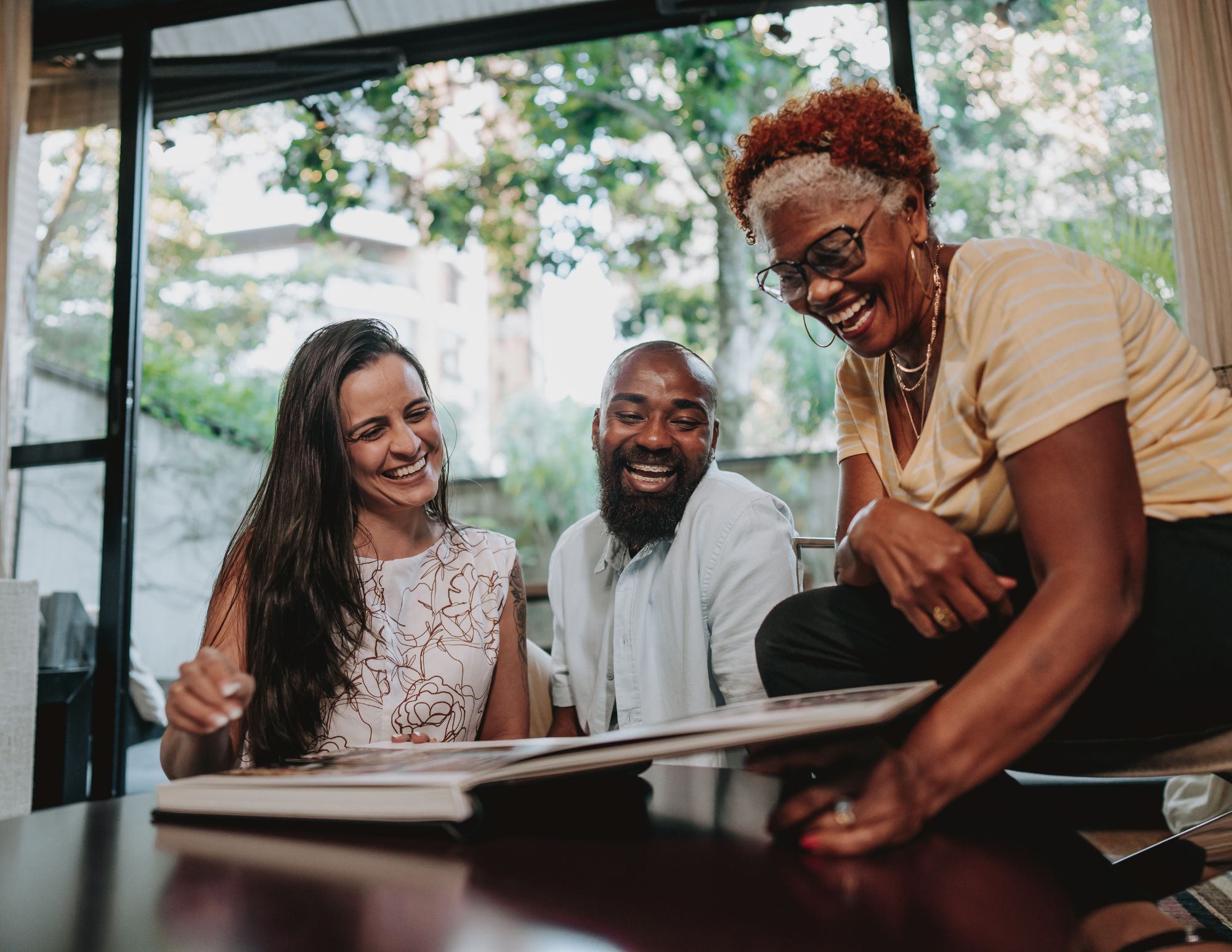 Married couple and mother laughing together while looking through the wedding photo album, warm and intimate moment.