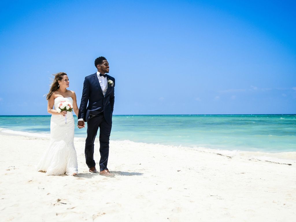 Couple de jeunes mariés marchant sur une plage des Caraïbes après leur cérémonie de mariage.