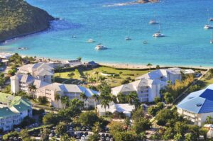 Vue aérienne du Domaine Anse Marcel Beach montrant l’hôtel, la plage privée et la baie turquoise entourée de collines.