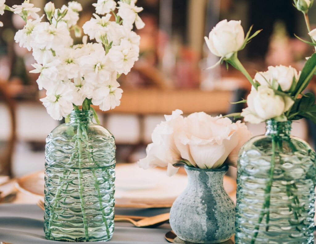 Zoom sur une décoration de table avec de petits vases verts contenant des fleurs blanches, alliant simplicité et raffinement.
